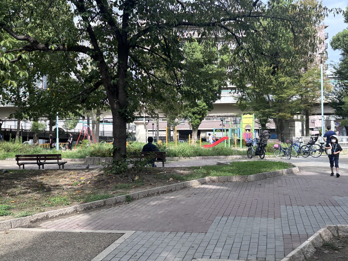 十三公園の風景。木陰のベンチと石畳の広場の奥に遊具が見える