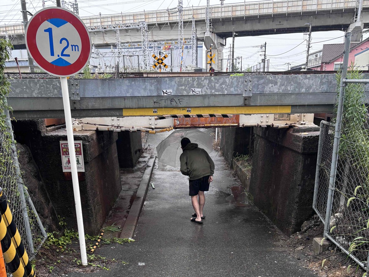 低い高架下を、少し頭をかがめて歩いて通る筆者